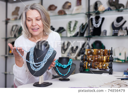 Woman trying on a turquoise necklace and earrings at a jewelry store 74856479