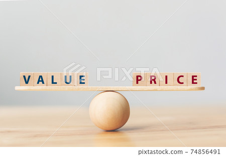 Wooden seesaw scale empty on wooden sphere on wood table with wording VALUE and PRICE balancing 74856491