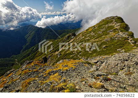 The west peak with clouds seen from the east peak of Mt. Shiomi in the Southern Alps in early autumn The west peak with clouds seen from the east peak of Mt. Shiomi in the Southern Alps in early autumn 74856622