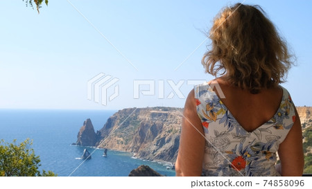 woman admires a beautiful view of the coast of the turquoise sea and mountains at Cape Fiolent 74858096