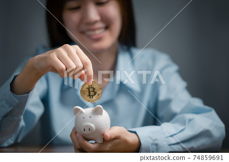Woman is putting golden bitcoin into the piggy bank. Woman is putting golden bitcoin into the piggy bank. 74859691