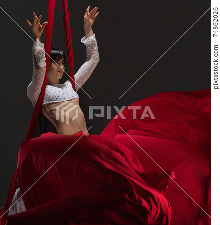 Pretty young gymnast on red aerial silks in studio 74862026