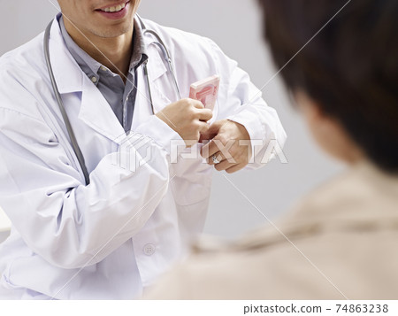 asian doctor putting kickback money in pocket 74863238