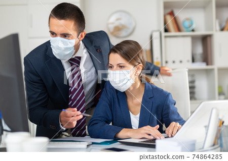Businessman with female colleague working in office in medical masks Businessman with female colleague working in office in medical masks 74864285
