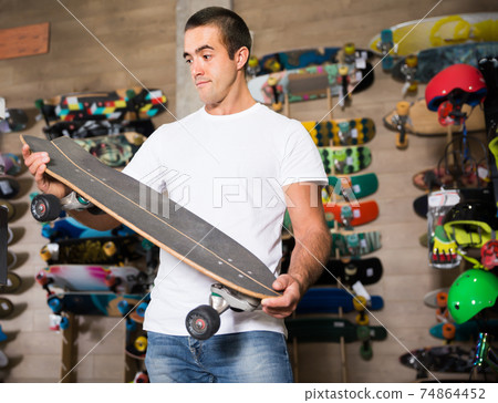 Positive young man choosing skateboard Positive young man choosing skateboard 74864452
