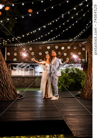 newlyweds with sparklers in night park with garlands in trees. ending to wedding 74864529