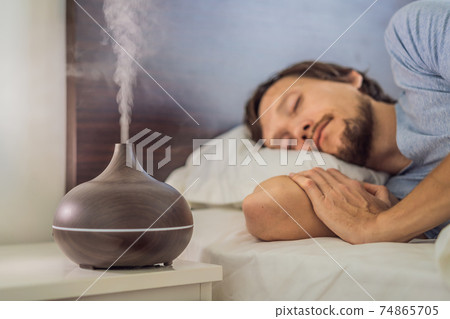 Aromatherapy Concept. Wooden Electric Ultrasonic Essential Oil Aroma Diffuser and Humidifier. Ultrasonic aroma diffuser for home. Man resting at home 74865705