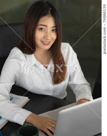 Businesswoman smiling to camera while working with laptop in office room 74866139