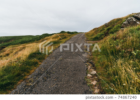Country road in a rural landscape amidst grass hills 74867240