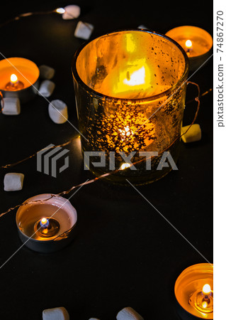 Candle lights. Burning candle on a dark background. Small marshmallows. Decorative and festive Christmas holiday arrangement with glasses and candles 74867270