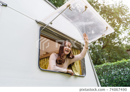 happy woman raising her hand at window of a camper RV van motorhome 74867490