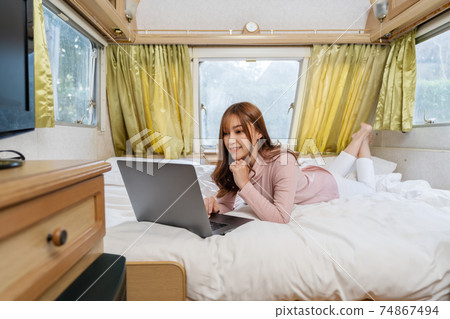 woman using laptop computer on bed of a camper RV van motorhome 74867494