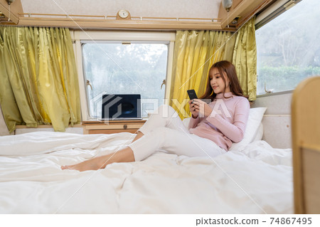 woman using smartphone on bed of a camper RV van motorhome 74867495