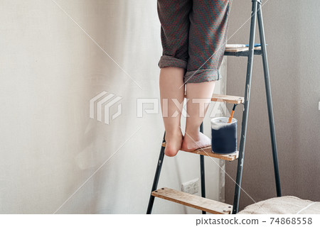 Woman with bare feet stained with white paint stands on stepladder. Home renovation concept Woman with bare feet stained with white paint stands on stepladder. Home renovation concept 74868558