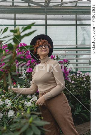 A beautiful plus size girl in a hat laughs among the green plants of greenhouse 74868638