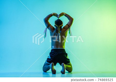 Young man thai boxer posing over blue background in neon light. 74869325