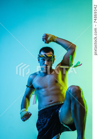 Portrait of young man thai boxer training over blue background. Portrait of young man thai boxer training over blue background. 74869342