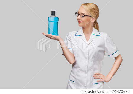 woman dentist doctor holding bottle of mouthwash standing over grey background woman dentist doctor holding bottle of mouthwash standing over grey background 74870681