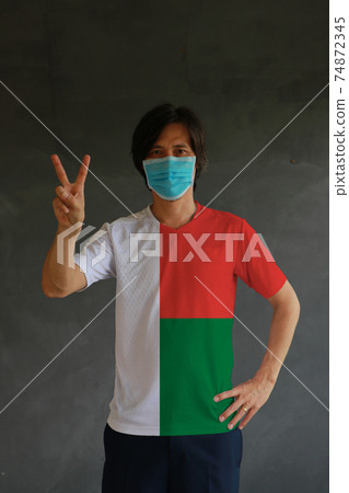 Man wearing hygienic mask and wearing Madagascar flag colored shirt and raising two fingers up Man wearing hygienic mask and wearing Madagascar flag colored shirt and raising two fingers up 74872345