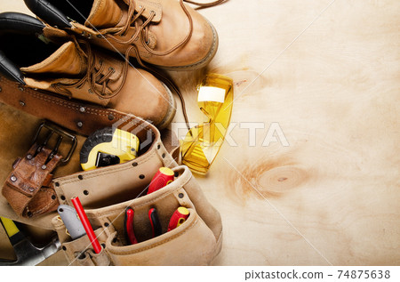 Construction concept background of toolbelt yellow boots goggles ant tools on plywood flat lay Construction concept background of toolbelt yellow boots goggles ant tools on plywood flat lay 74875638