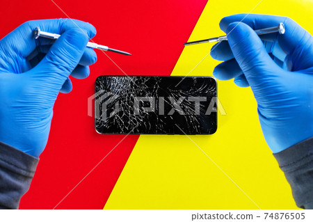 Repair of a cell phone.The hands of a master in gloves with screwdrivers over a broken smartphone Repair of a cell phone.The hands of a master in gloves with screwdrivers over a broken smartphone 74876505