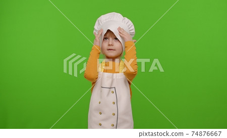 Child girl kid dressed as professional cook chef smiling, crosses arms and looks intently at camera 74876667