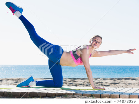 Joyful woman stretching muscles on the sand 74878059