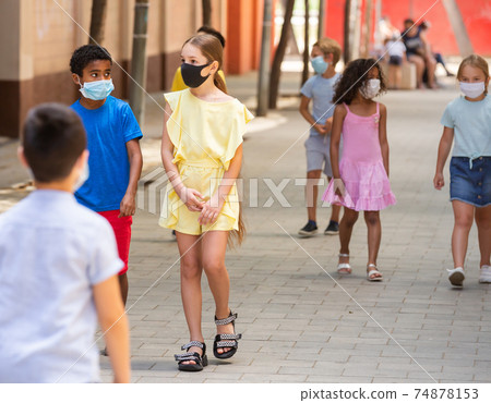 Group of children in protective medical masks walking on street in fine weather 74878153