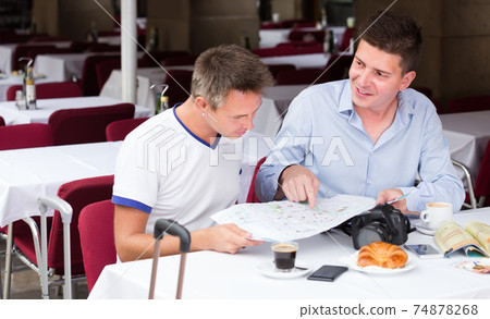 two young men sitting with coffee and looking at map in cafe two young men sitting with coffee and looking at map in cafe 74878268