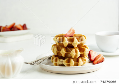 Delicious breakfast. Belgian waffles with honey and strawberries. Cup of tea white wooden background, top view. Delicious breakfast. Belgian waffles with honey and strawberries. Cup of tea white wooden background, top view. 74879066