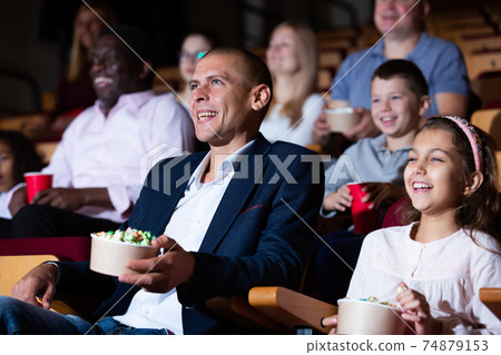 Cheerful family watching a movie and eating popcorn in cinema Cheerful family watching a movie and eating popcorn in cinema 74879153