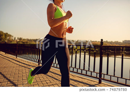 A sports girl runs through the park by the lake. 74879780