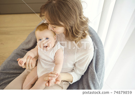 A mother with a baby in her arms sitting on a chair in front of 74879859