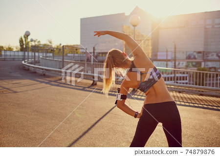 A runner girl makes a warm-up before jogging in the autumn. 74879876