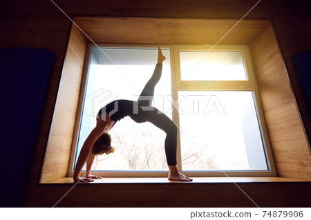 Woman doing yoga bridge on the background window. Exercising at 74879906
