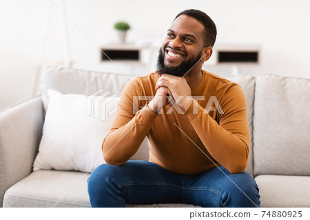 Happy African Guy Thinking Dreaming Sitting On Sofa At Home Happy African Guy Thinking Dreaming Sitting On Sofa At Home 74880925