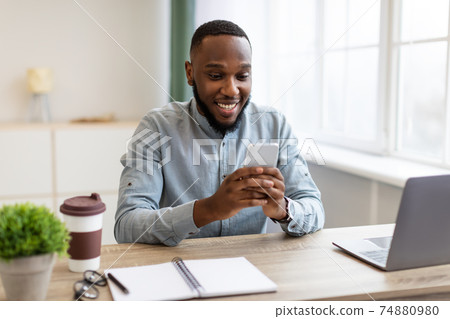 Happy African Businessman Using Phone App Sitting At Workplace Indoors Happy African Businessman Using Phone App Sitting At Workplace Indoors 74880980
