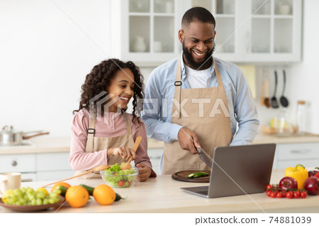 Black man and girl cooking in the kitchen reading recipe Black man and girl cooking in the kitchen reading recipe 74881039