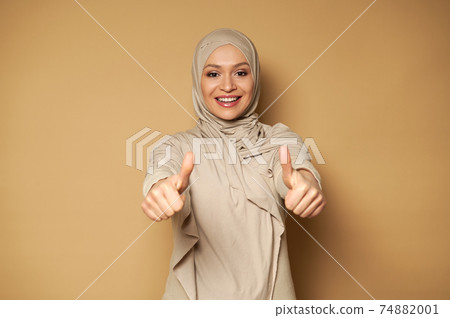 Beautiful Muslim woman in hijab cute smiling with toothy smile and showing thumbs up while looking to the camera 74882001