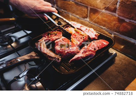 Hand turns steak with tongs during preparation on the grill pan with seasonings Hand turns steak with tongs during preparation on the grill pan with seasonings 74882718