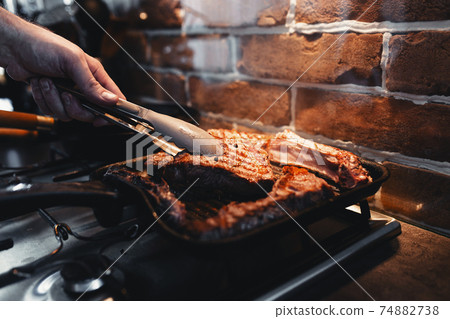 Hand turns steak with tongs during preparation on the grill pan with seasonings 74882738