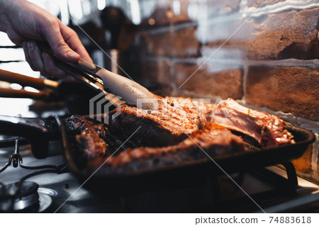 Hand turns steak with tongs during preparation on the grill pan with seasonings 74883618