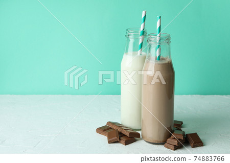 Bottles with milk and milkshake, and chocolate pieces against mint background 74883766