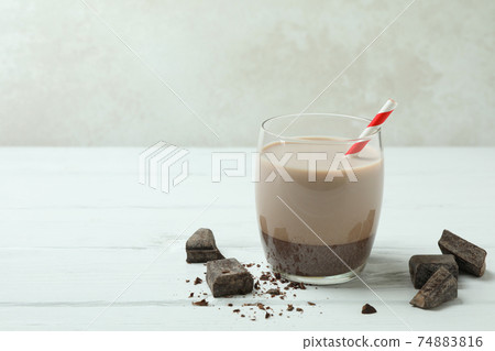 Glass of chocolate milkshake and chocolate pieces on white wooden table 74883816
