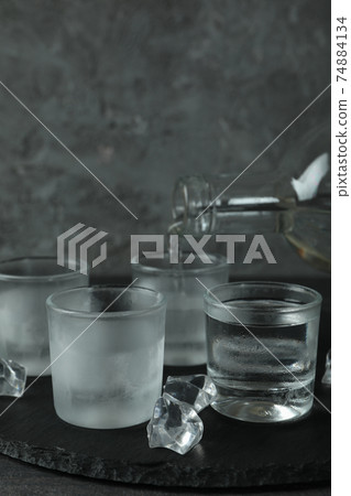 A bottle with pouring vodka and shots of vodka on black tray A bottle with pouring vodka and shots of vodka on black tray 74884134
