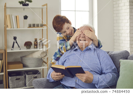 Happy smiling little grandson covers grandfather's eyes and plays Guess Who game Happy smiling little grandson covers grandfather's eyes and plays Guess Who game 74884450