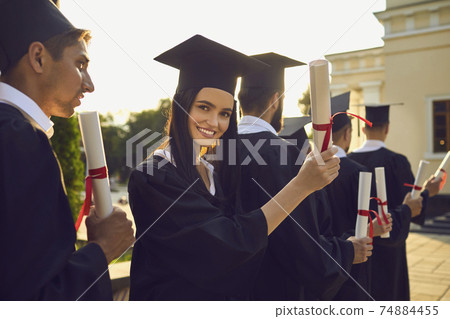 Smiling pretty girl student university graduate holding diploma with honors in hand Smiling pretty girl student university graduate holding diploma with honors in hand 74884455