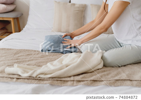 Woman sitting on bed and organizing fall and winter warm clothing. 74884872