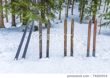 Old wooden skis stuck in the snow in the forrest. Vintage winter sports background. 74884934