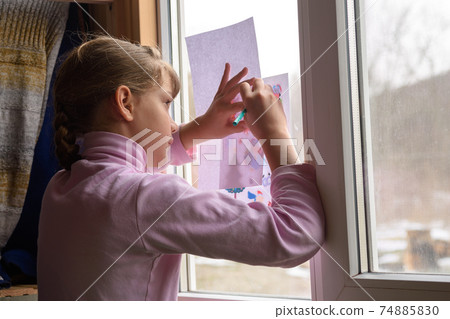 The girl copies the printed picture onto a blank sheet by attaching the picture to the window glass 74885830